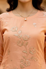 Close-up of a peach-colored top with floral embroidery and a pearl necklace. Product by Umaid Couture