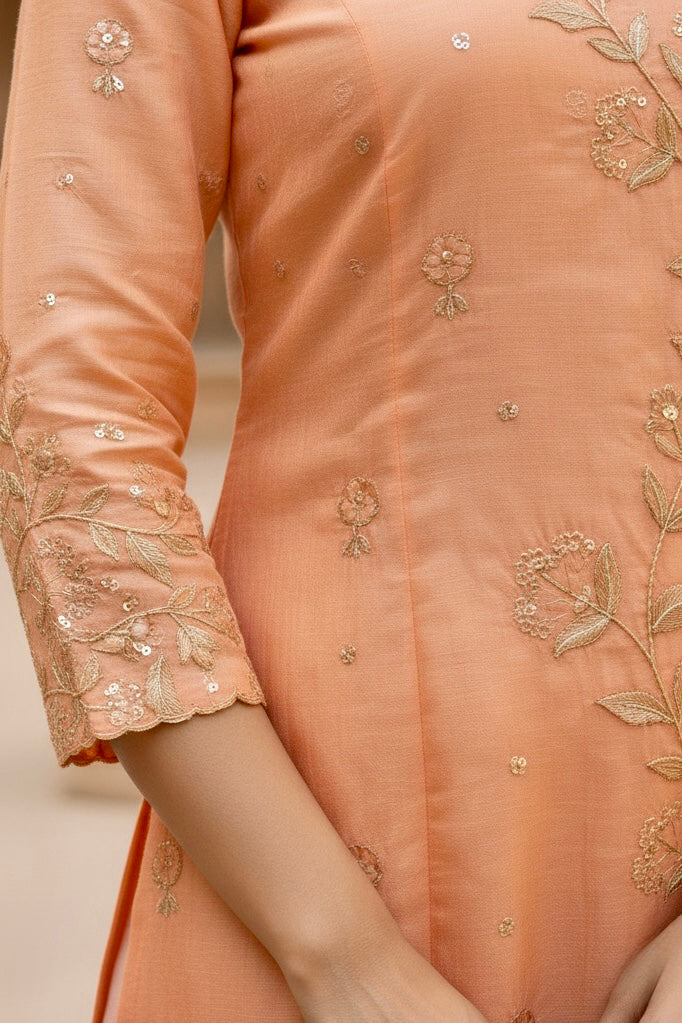Close-up of a peach-colored outfit with floral embroidery on a neutral background. Product by Umaid Couture