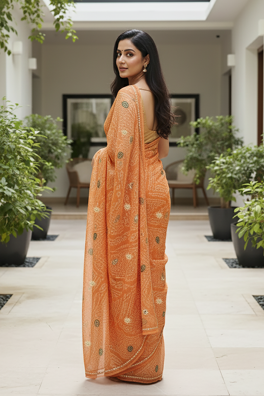 Woman in an Bandhej saree by Umaid Couture standing in a well-lit indoor setting with plants.