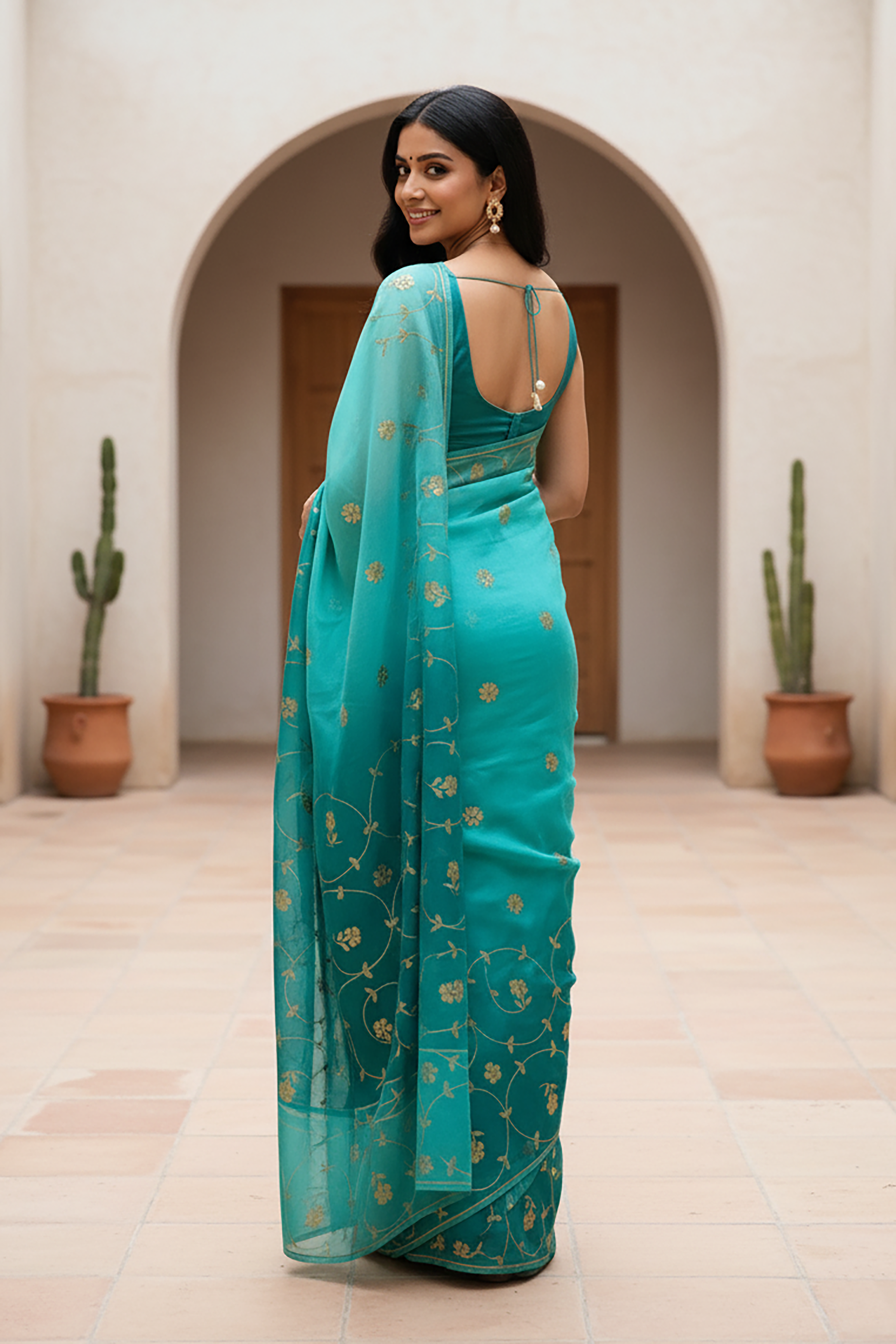 Woman wearing a teal saree by Umaid Couture with gold patterns in an indoor setting.