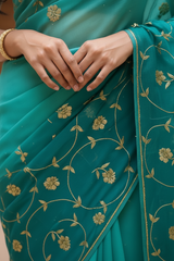 Woman wearing a teal saree by Umaid Couture with gold patterns in an indoor setting.