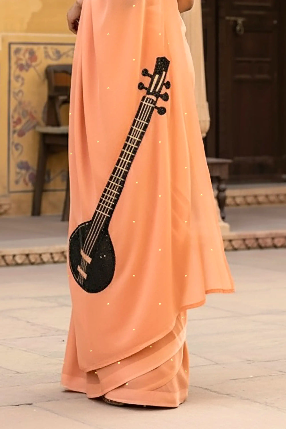 A woman in peach saree embellished with Sitar motif by Umaid Couture