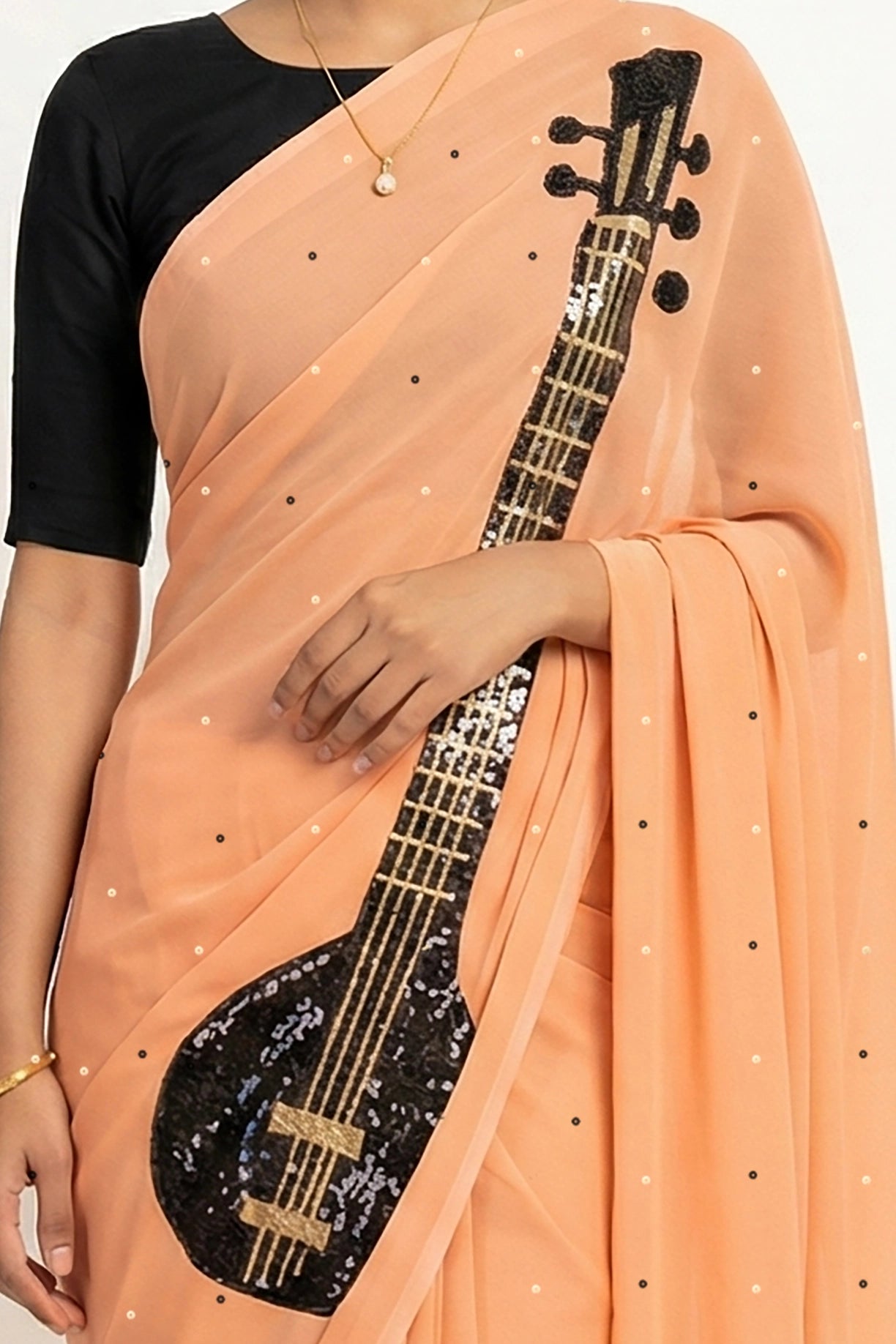 An Indian woman in peach Ragini Saree embellished  with Sitar Motifs made of Zari & sequins by craft of Aari-Zardosi, a product of Umaid Couture