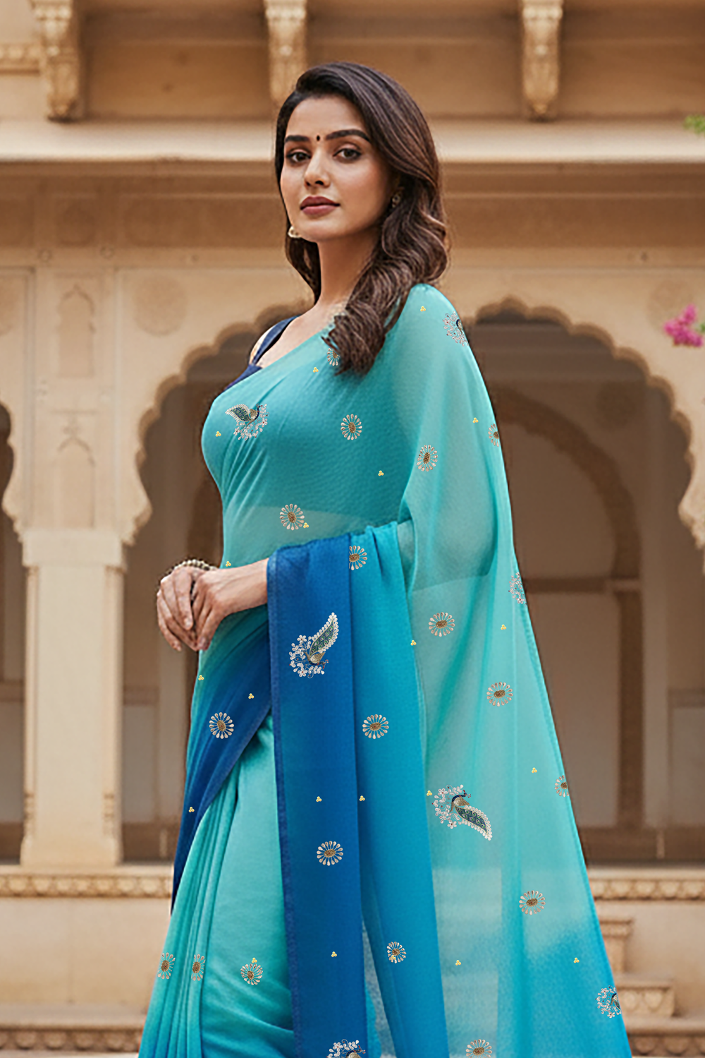 Woman standing in front of an architectural background wearing a gradient Blue saree embellished with Peacock motifs by Umaid Couture
