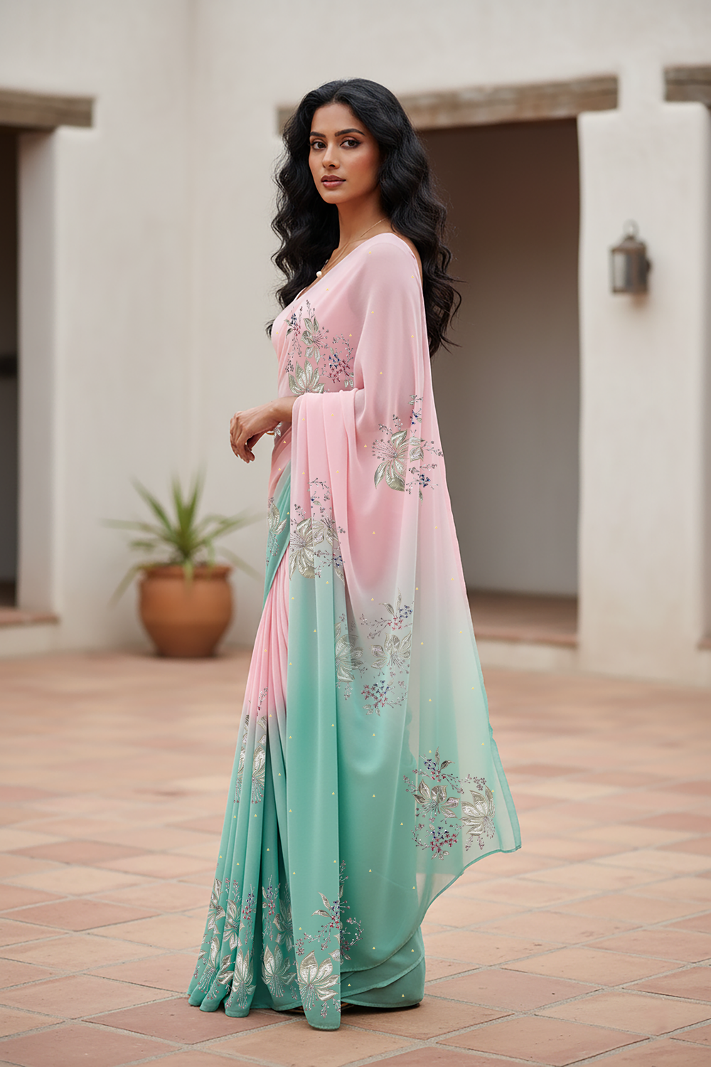 Woman wearing a gradient pastel pink and sea green chiffon saree by Umaid Couture, standing in a minimal courtyard.