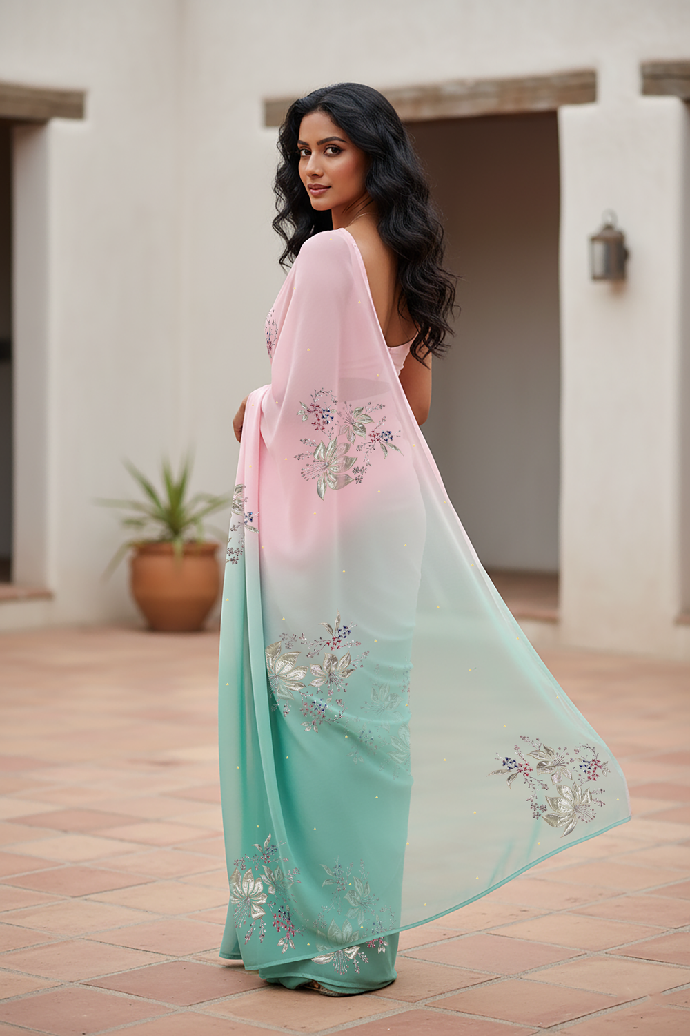 Woman wearing a gradient pastel pink and sea green chiffon saree by Umaid Couture, standing in a minimal courtyard.