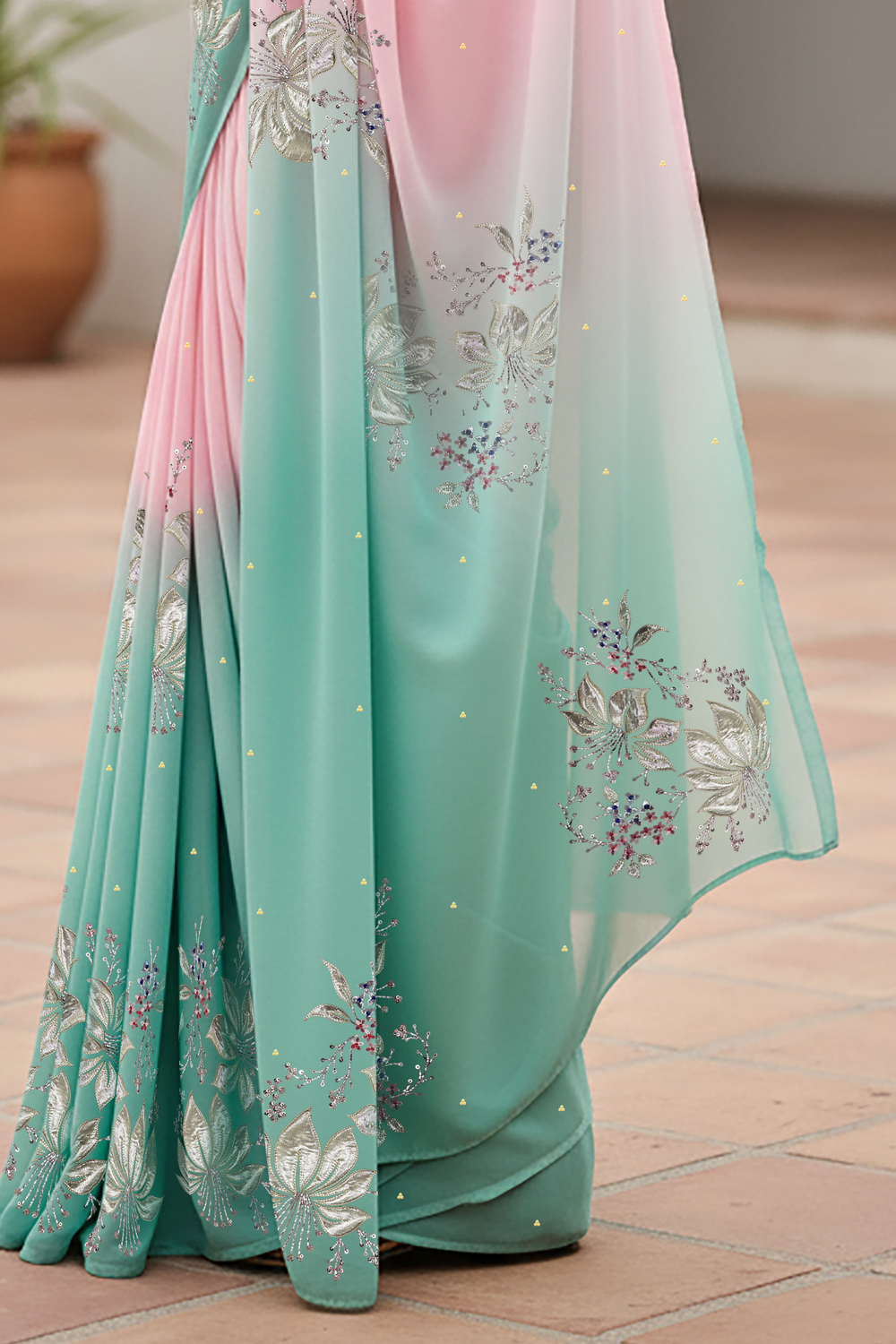 Woman wearing a gradient pastel pink and sea green chiffon saree by Umaid Couture, standing in a minimal courtyard.