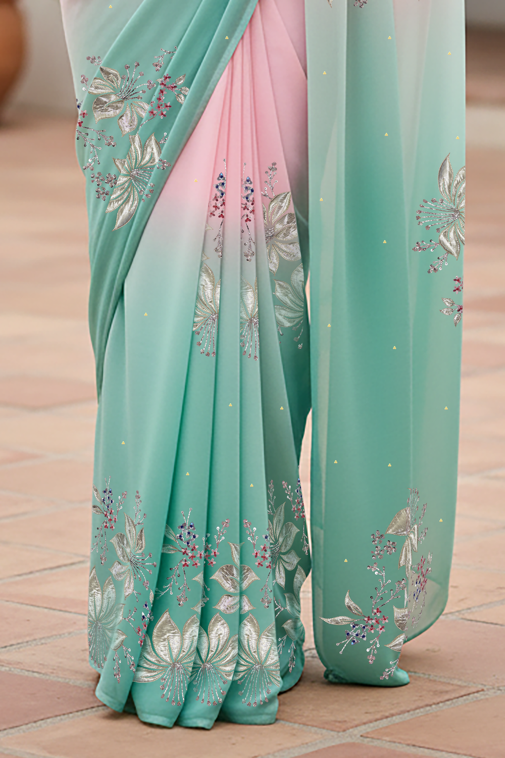 Woman wearing a gradient pastel pink and sea green chiffon saree by Umaid Couture, standing in a minimal courtyard.