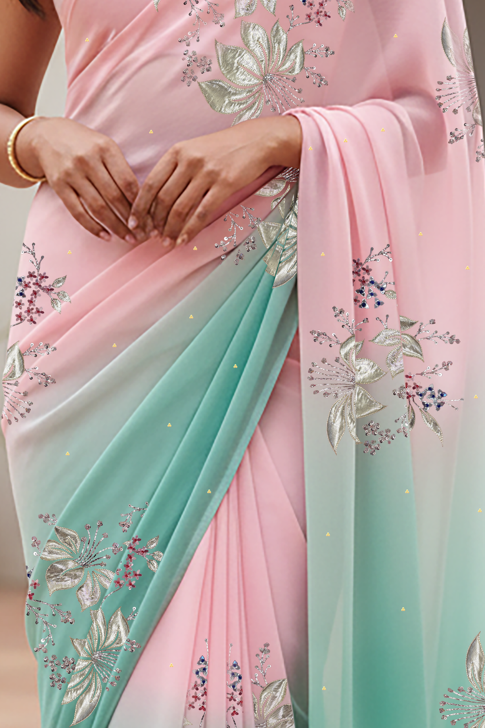Woman wearing a gradient pastel pink and sea green chiffon saree by Umaid Couture, standing in a minimal courtyard.