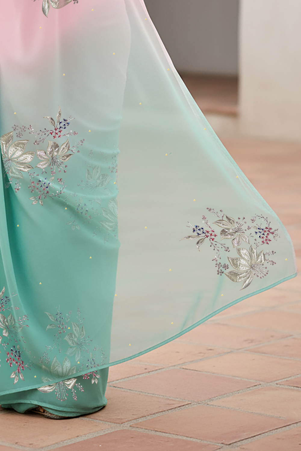 Woman wearing a gradient pastel pink and sea green chiffon saree by Umaid Couture, standing in a minimal courtyard.
