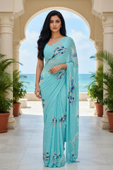 An Indian woman standing in a seaside hotel courtyard wearing sea green color chiffon saree embellished with blue, pink, cyan and sliver sequin of fish motifs by Umaid Couture.  
