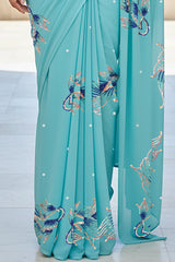 An Indian woman standing in a seaside hotel courtyard wearing sea green color chiffon saree embellished with blue, pink, cyan and sliver sequin of fish motifs by Umaid Couture.  
