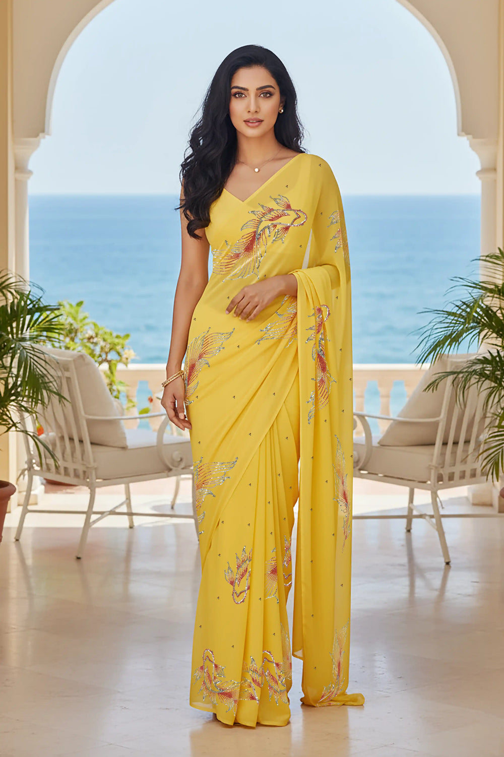Woman in a yellow saree with fish Motifs in sequins by umaid couture standing in a room with a view of the ocean.
