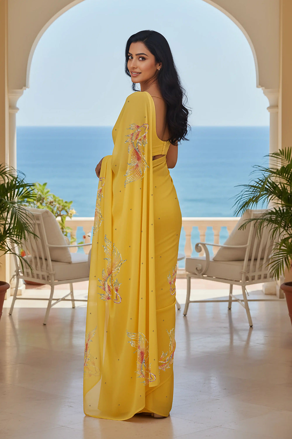 Woman in a yellow saree with fish Motifs in sequins by umaid couture standing in a room with a view of the ocean.