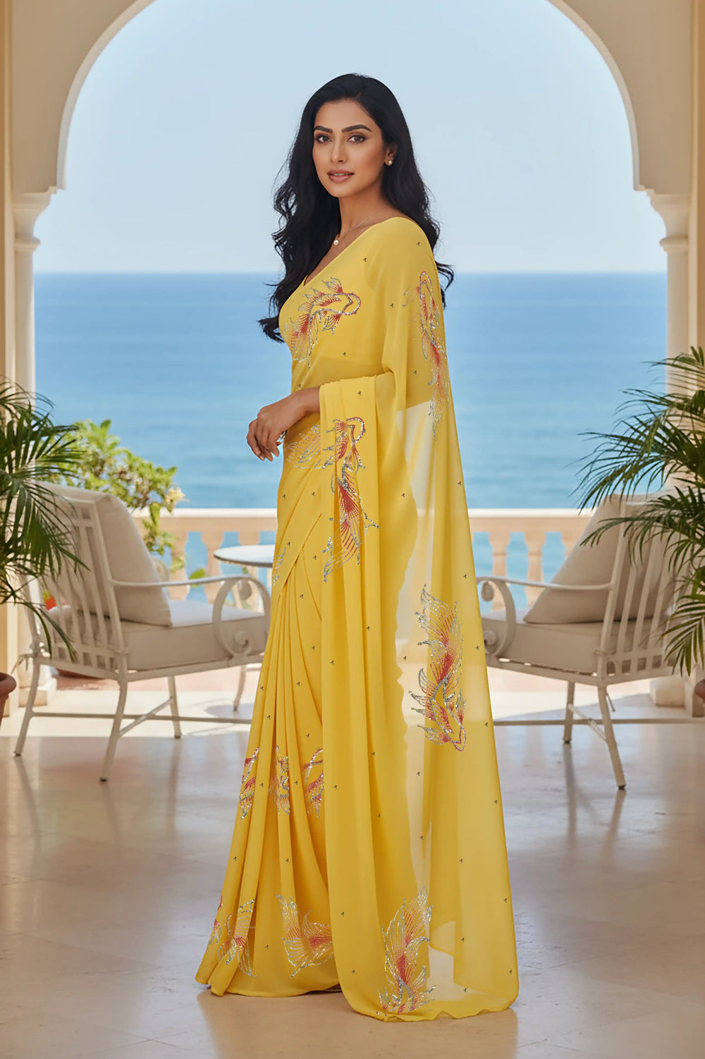 Woman in a yellow saree with fish Motifs in sequins by umaid couture standing in a room with a view of the ocean.
