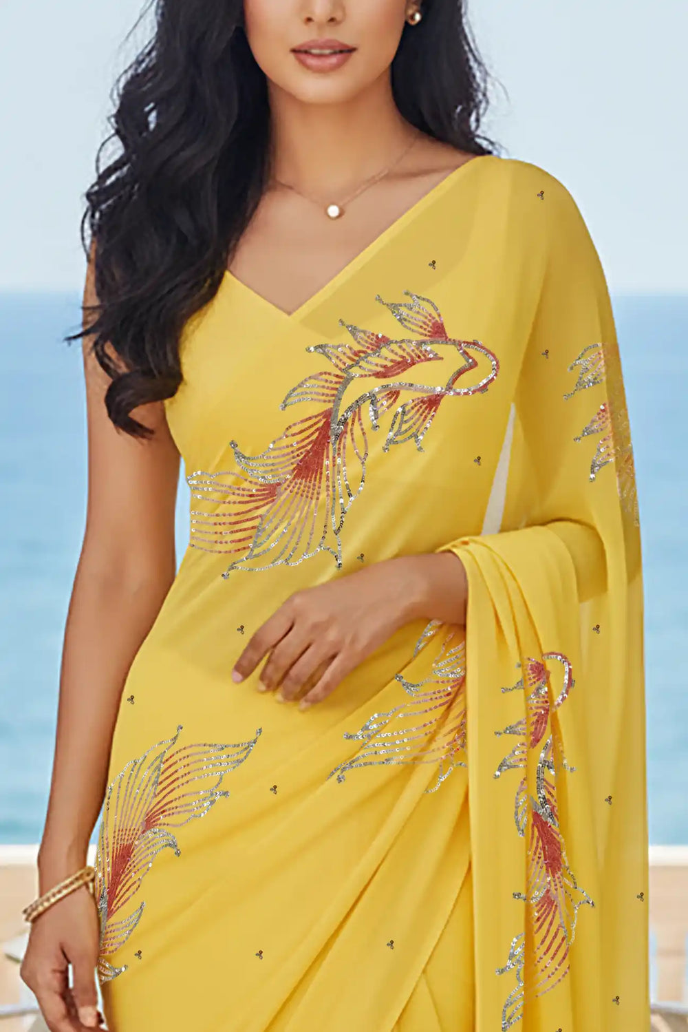 Woman in a yellow saree with fish Motifs in sequins by umaid couture standing in a room with a view of the ocean.