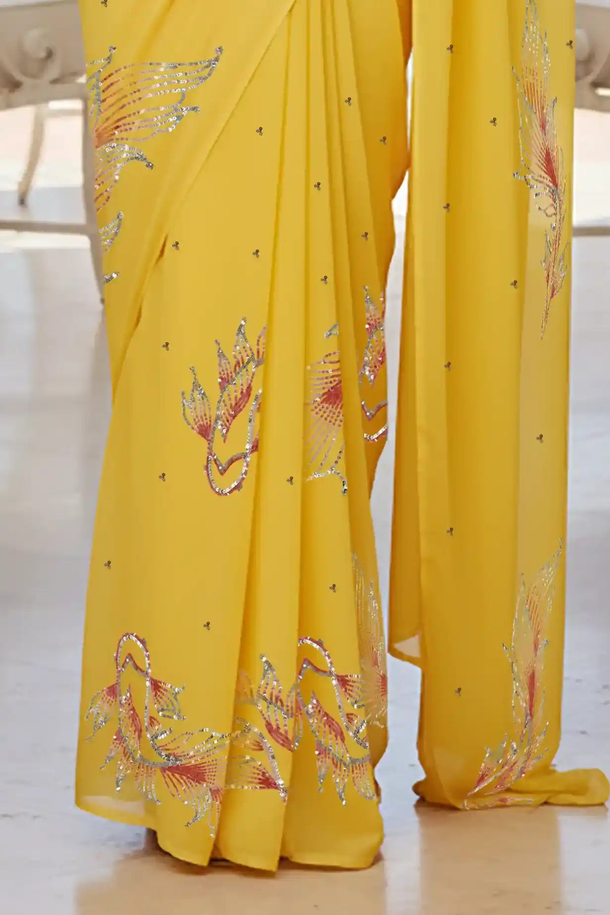 Woman in a yellow saree with fish Motifs in sequins by umaid couture standing in a room with a view of the ocean.