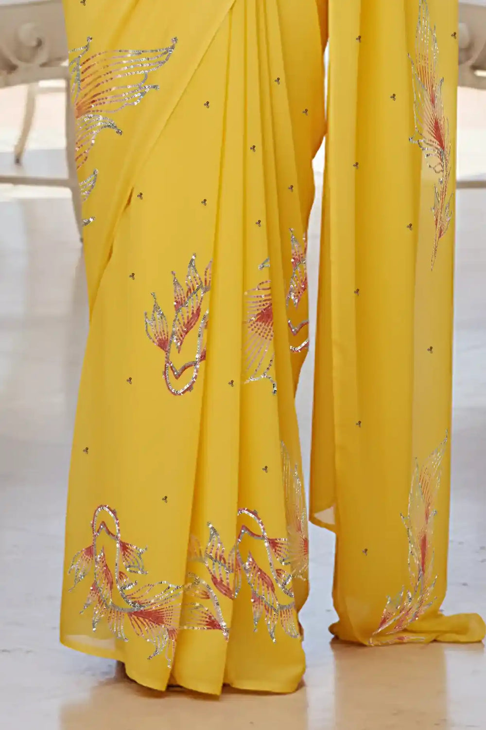 Woman in a yellow saree with fish Motifs in sequins by umaid couture standing in a room with a view of the ocean.