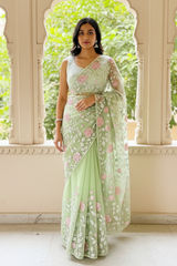 Woman in a light green saree with floral patterns by Umaid Couture standing in a decorative indoor setting.