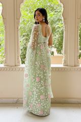 Woman in a light green saree with floral patterns by Umaid Couture standing in a decorative indoor setting.