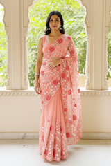 Woman wearing a pink floral saree by Umaid Couture standing in front of an archway with greenery.