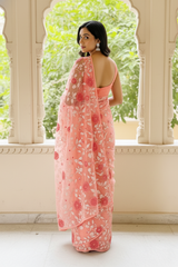 Woman wearing a pink floral saree by Umaid Couture standing in front of an archway with greenery.