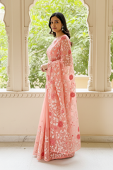 Woman wearing a pink floral saree by Umaid Couture standing in front of an archway with greenery.