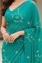 Teal saree with floral patterns worn by a person, blurred background