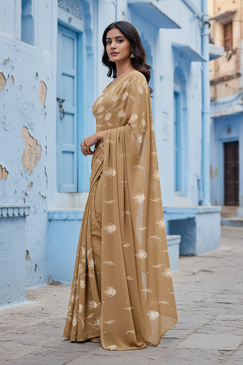 Woman in a beige saree standing in an architectural setting with plants and arches. Product by Umaid Couture