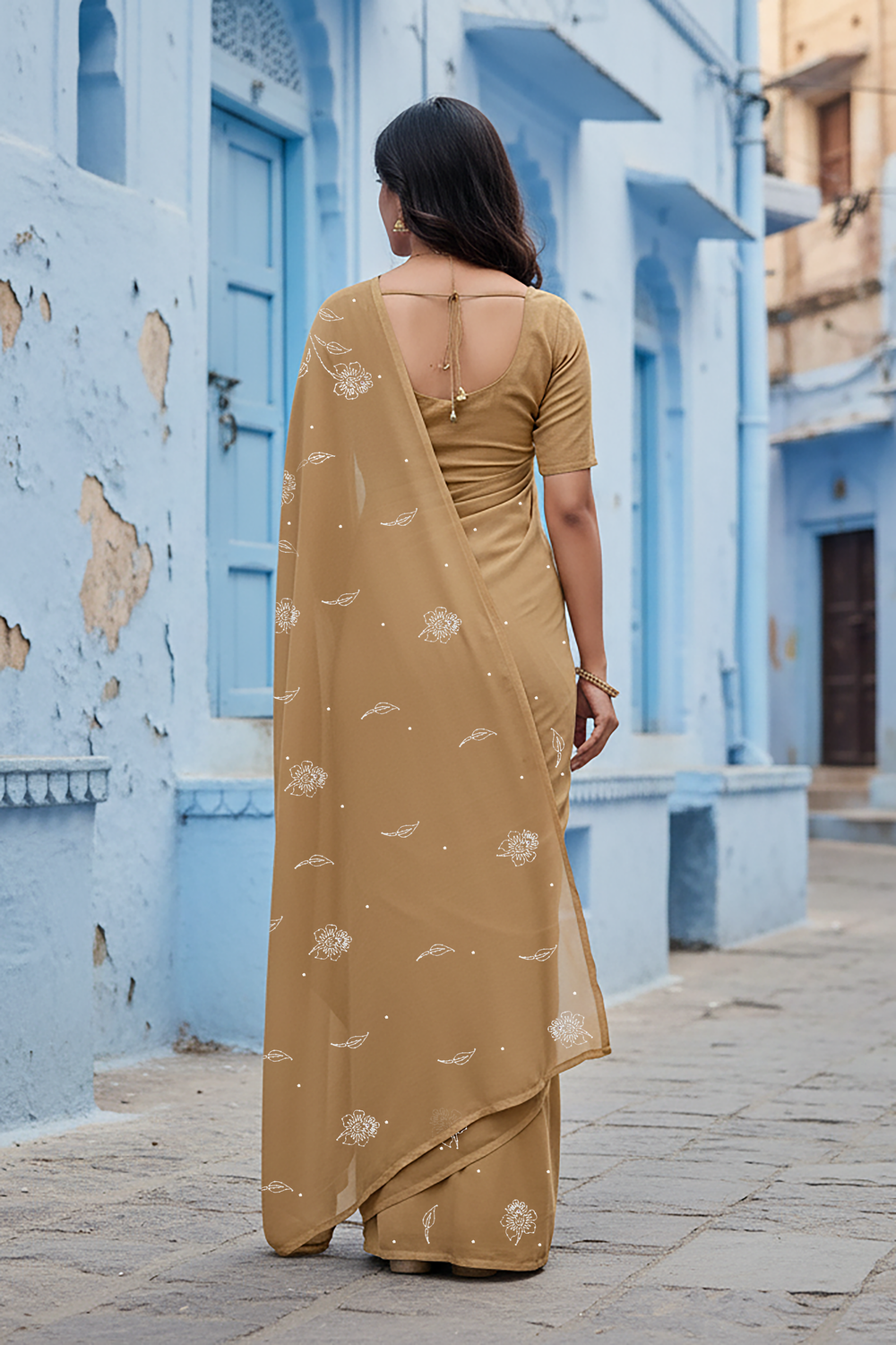 Woman in a beige saree standing in front of an architectural structure with plants around. Product by Umaid Couture