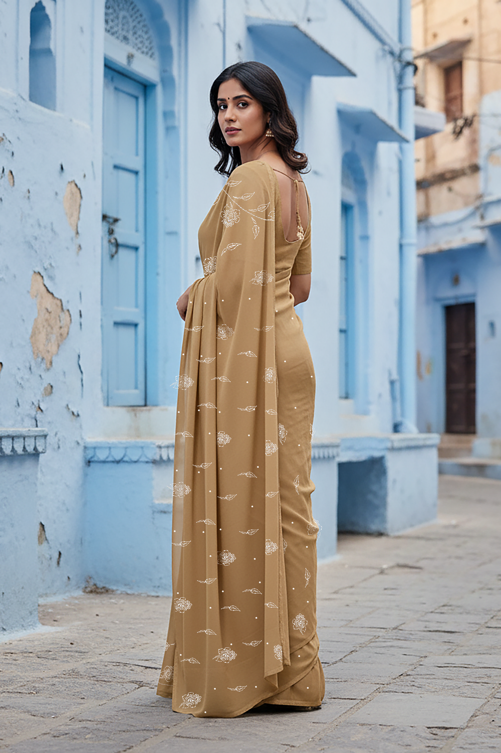 Woman in a beige saree standing in front of an architectural background. Product by Umaid Couture