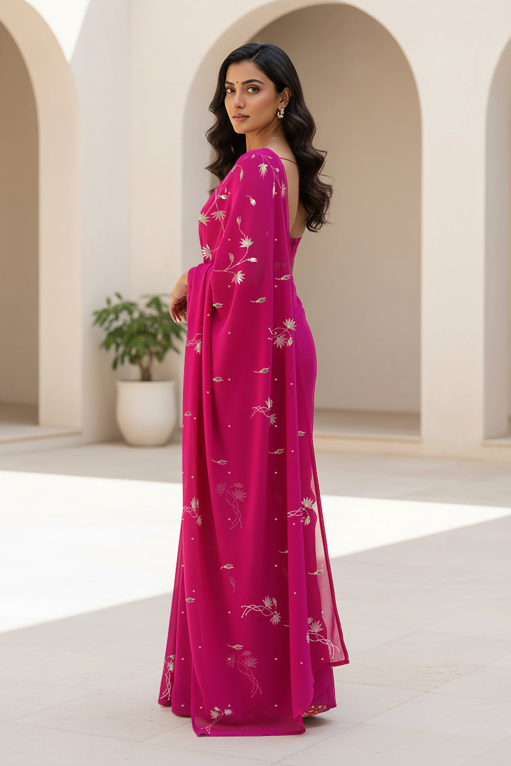 Woman in a pink saree with floral patterns standing in an archway. Product By Umaid Couture
