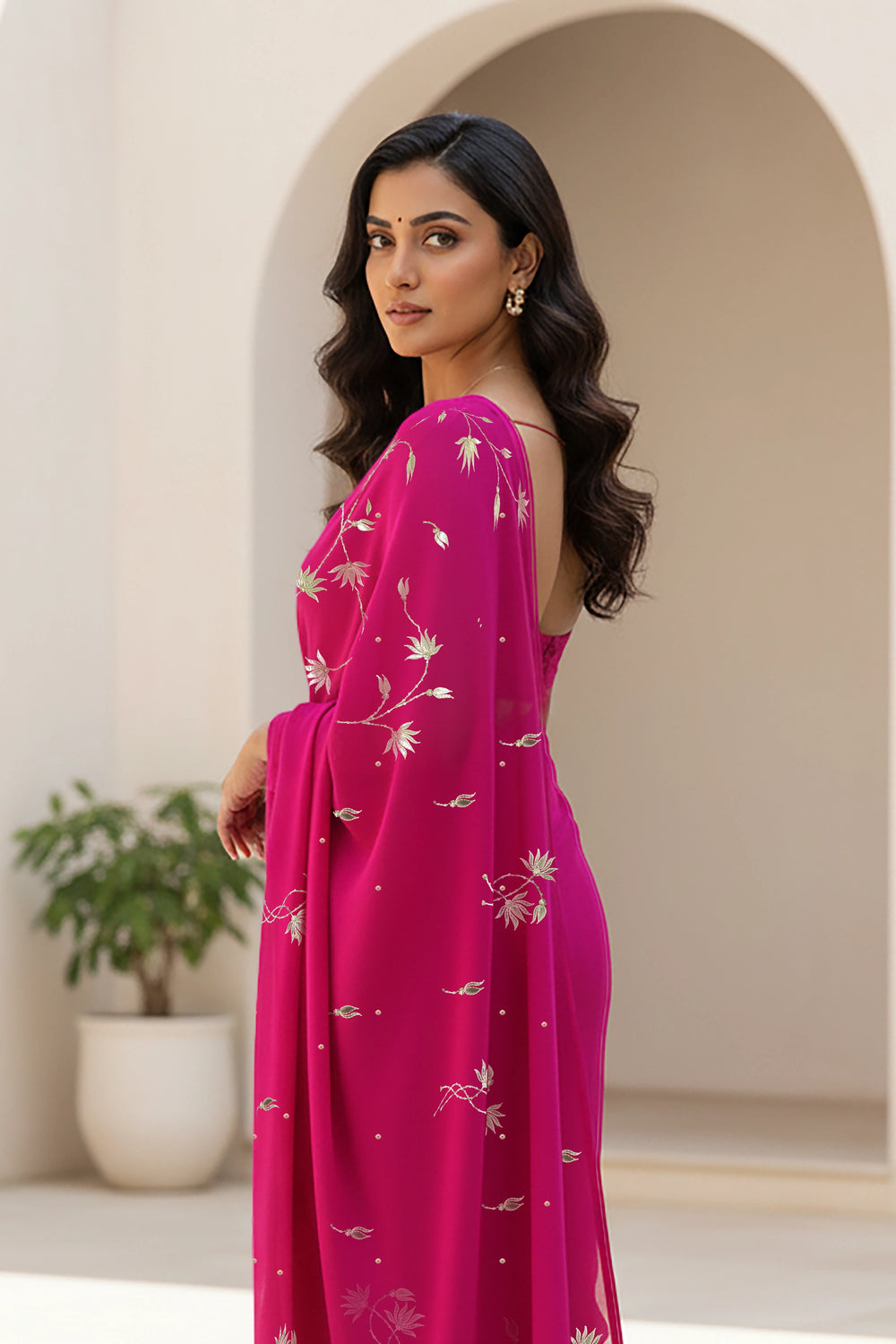 Woman in a pink dress with floral patterns standing in a neutral-colored room. Product By Umaid Couture