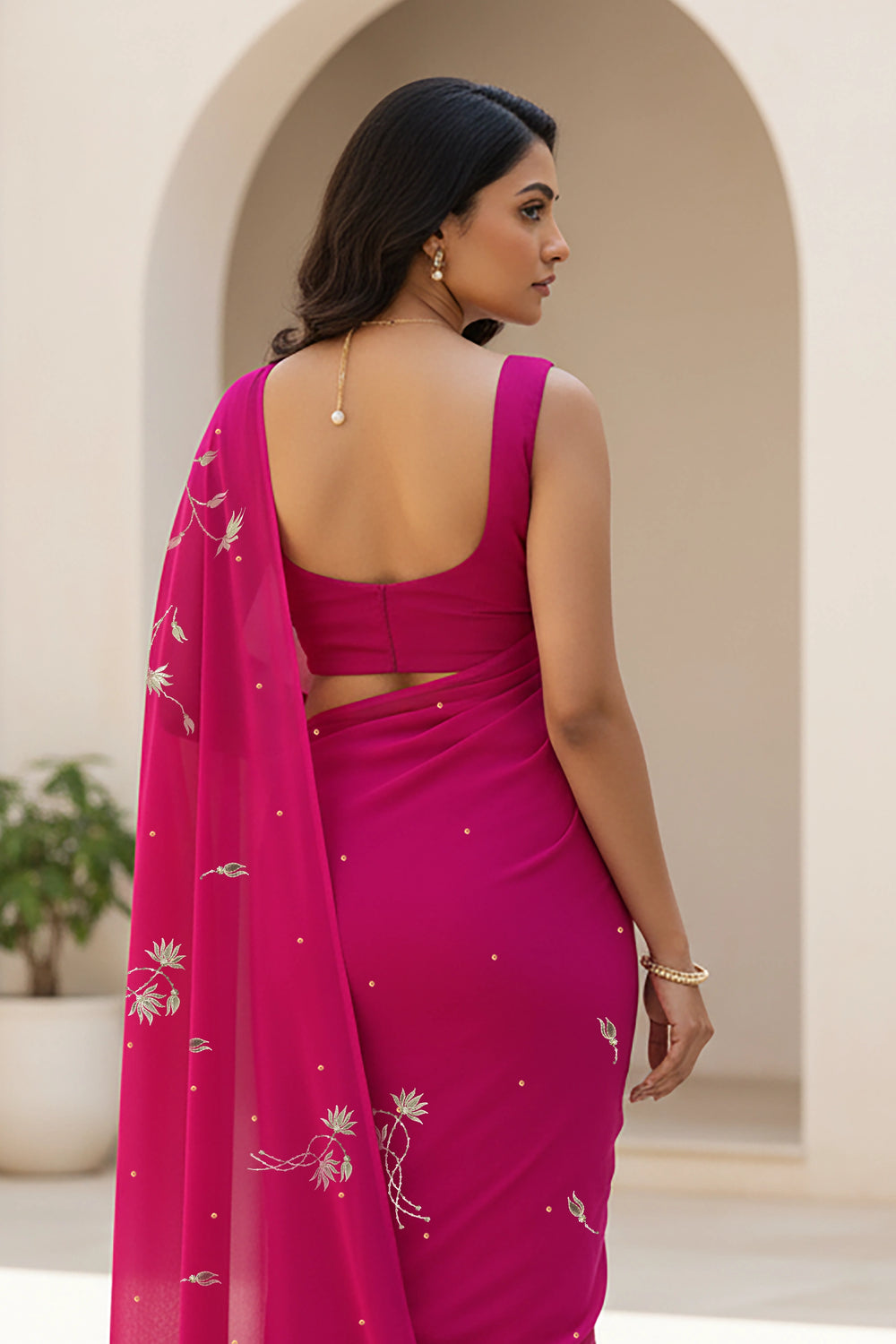 Woman wearing a bright pink saree with a matching blouse, standing in an outdoor setting. Product By Umaid Couture