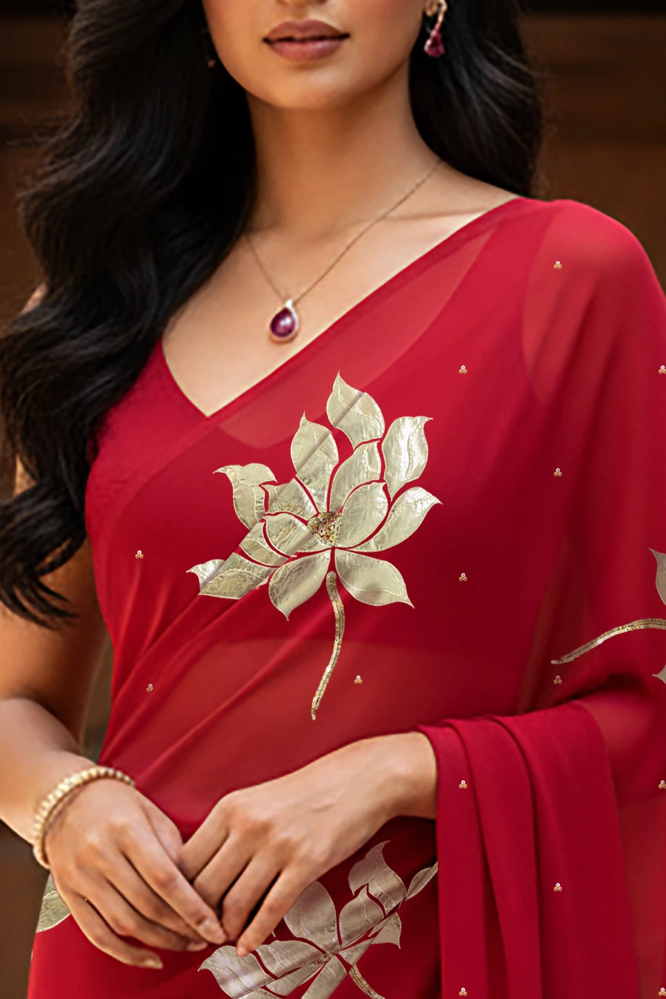 An Indian woman standing in a garden courtyard wearing red chiffon saree embellished with large gota lotus flower motifs by Umaid Couture.  
