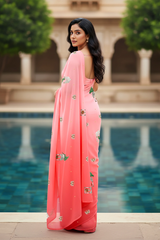 An Indian woman standing in a garden courtyard wearing a gradient of pink chiffon saree embellished with green and sliver sequin of l parrot siting in heritage style window motifs by Umaid Couture.  
