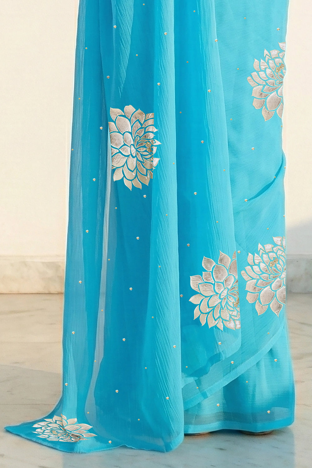 An Indian woman in Middle Blue Dahlia Saree embellished with Blooming Dahlia flowers made of Gota, Zari & sequins by craft of Aari-Zardosi, a product of Umaid Couture