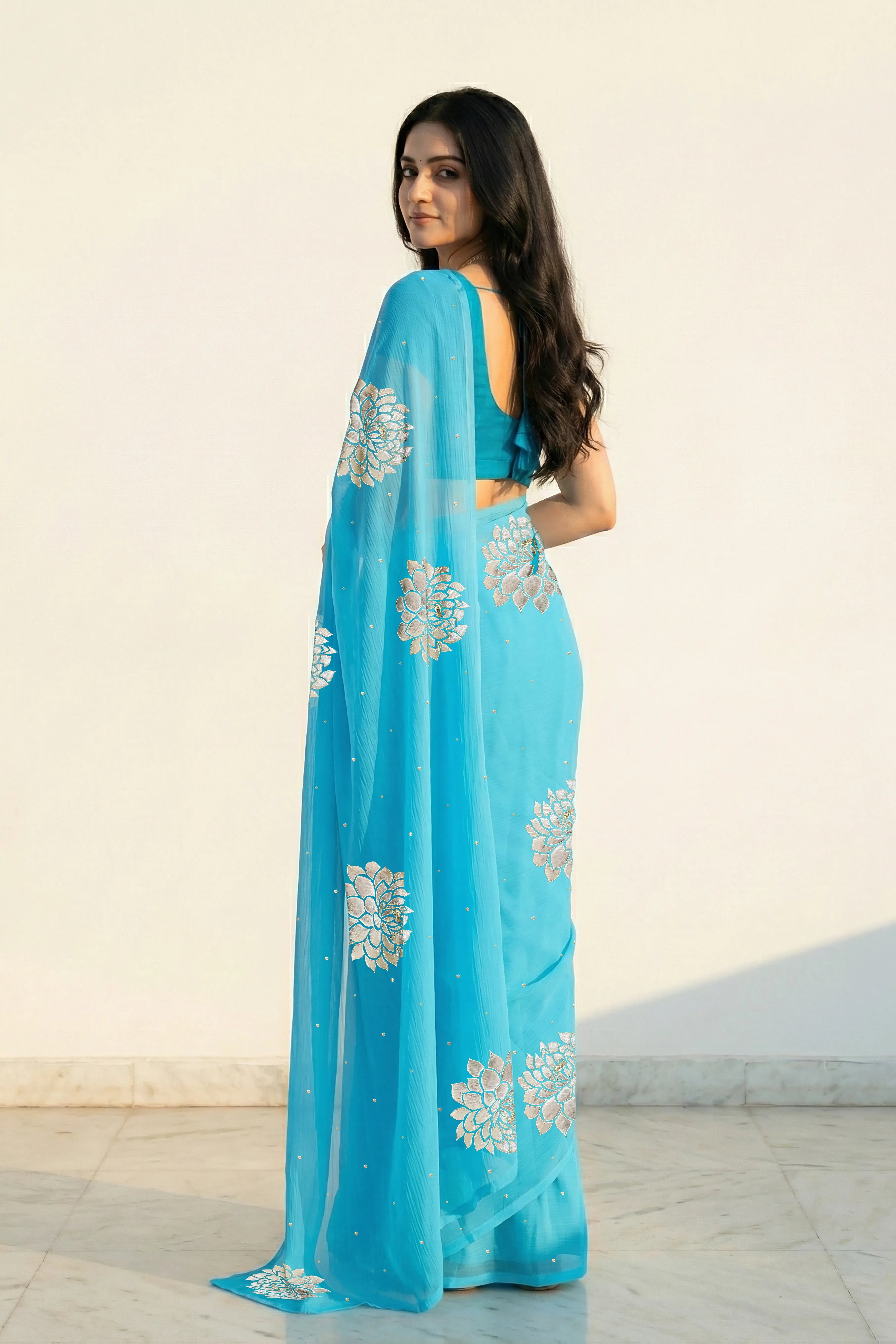 An Indian woman in Middle Blue Dahlia Saree embellished with Blooming Dahlia flowers made of Gota, Zari & sequins by craft of Aari-Zardosi, a product of Umaid Couture