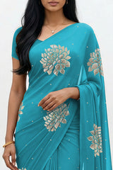 An Indian woman standing in a minimal white courtyard wearing a middle blue chiffon saree embellished with golden and sliver sequin of Dahlia flower motifs by Umaid Couture.  
