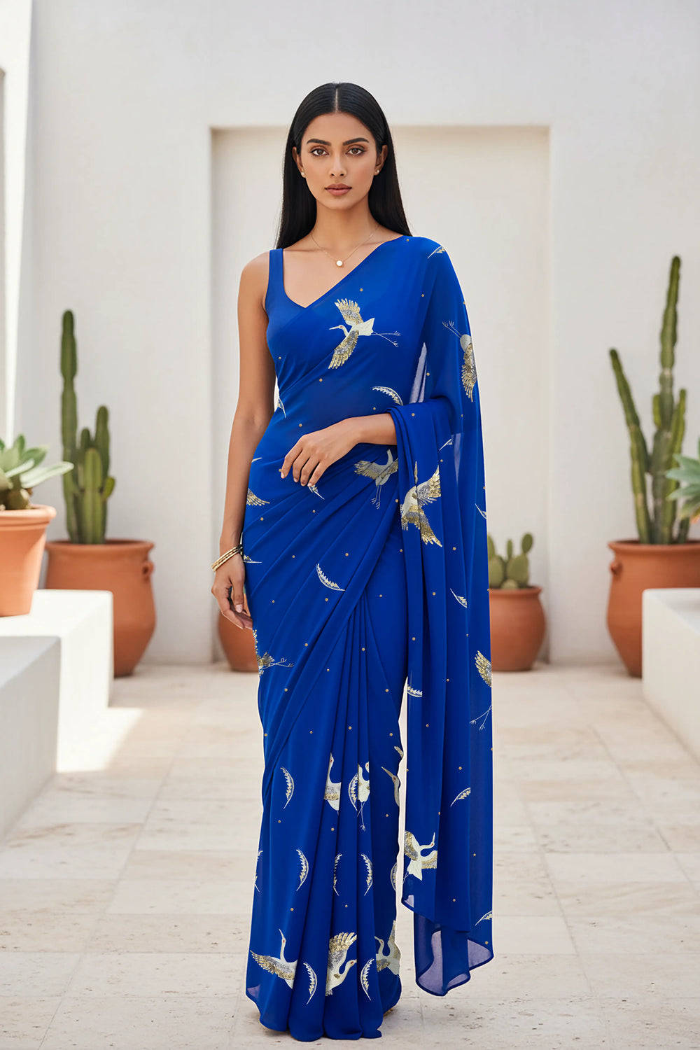 An Indian woman standing in a minimal Mexican courtyard wearing a revolutionary blue chiffon saree embellished with kurta bird motifs made with  shimmering Zari, Resham, Sequins, and Aari-Zardosi craft by Umaid Couture.  
