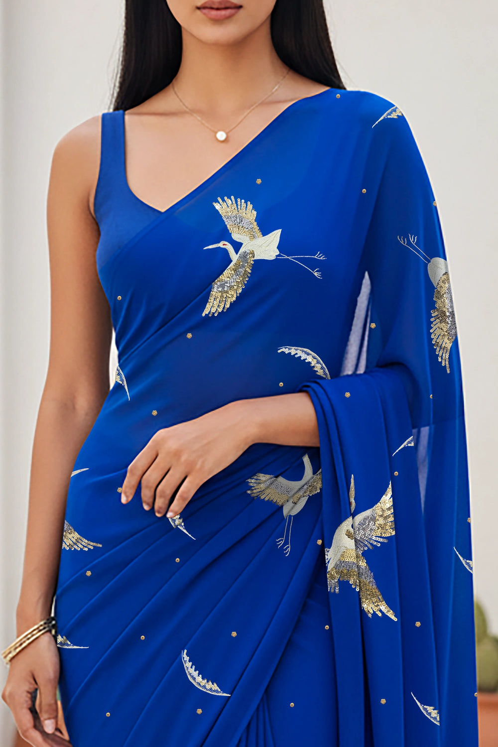 An Indian woman standing in a minimal Mexican courtyard wearing a revolutionary blue chiffon saree embellished with kurta bird motifs made with  shimmering Zari, Resham, Sequins, and Aari-Zardosi craft by Umaid Couture.  
