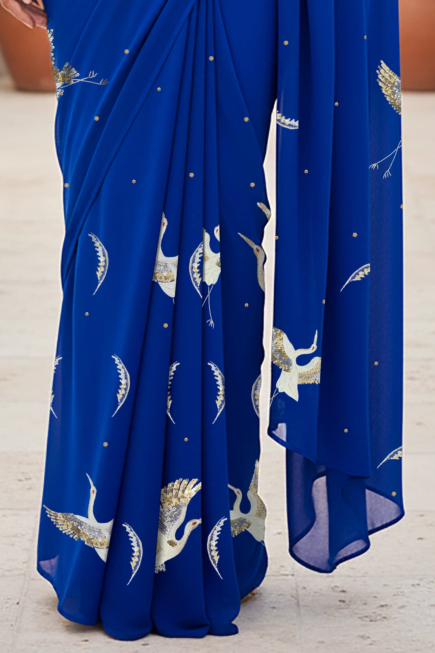 An Indian woman standing in a minimal Mexican courtyard wearing a revolutionary blue chiffon saree embellished with kurta bird motifs made with  shimmering Zari, Resham, Sequins, and Aari-Zardosi craft by Umaid Couture.  
