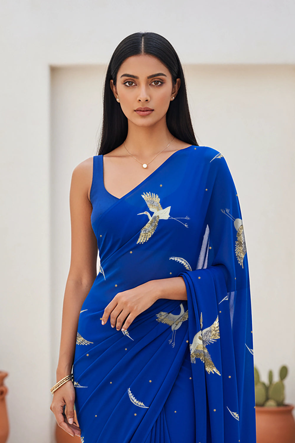 An Indian woman standing in a minimal Mexican courtyard wearing a revolutionary blue chiffon saree embellished with kurta bird motifs made with  shimmering Zari, Resham, Sequins, and Aari-Zardosi craft by Umaid Couture.  
