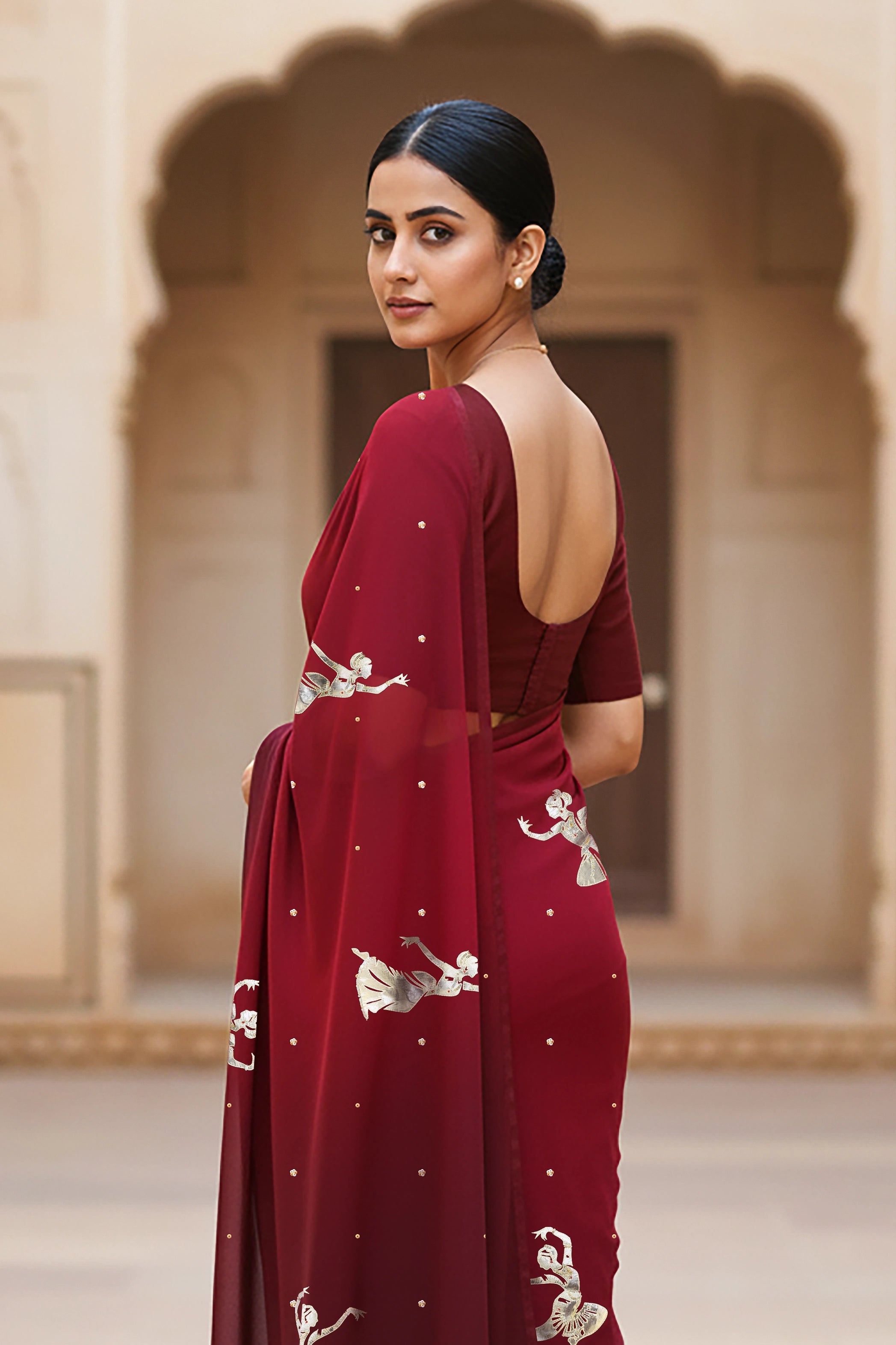 woman standing wearing wine red hue mulberry chiffon silk saree with kathak dance motifs on it designed bt umaid couture.