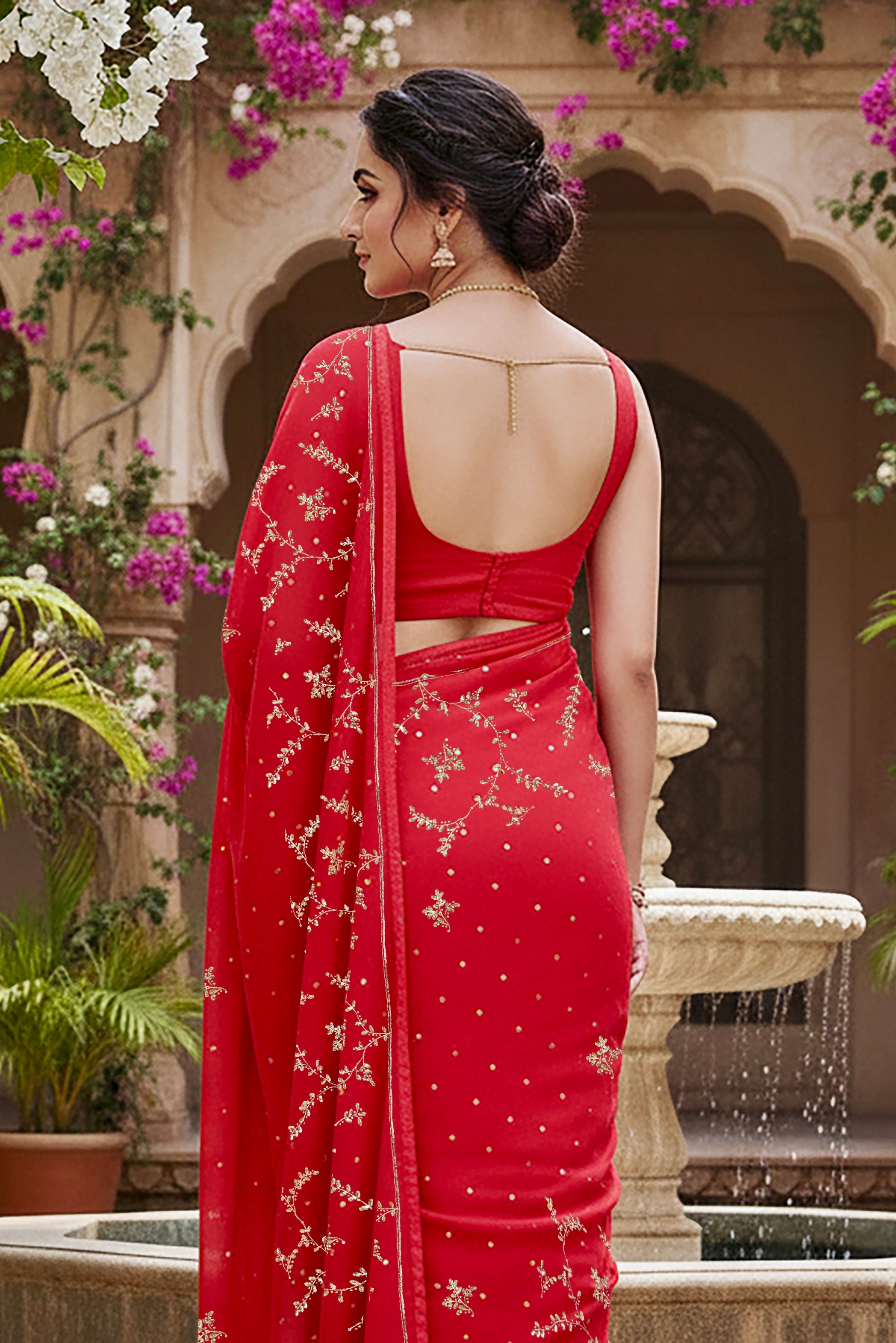 A model wearing a vibrant red gulmohar glow saree by umaid couture, standing in a garden courtyard