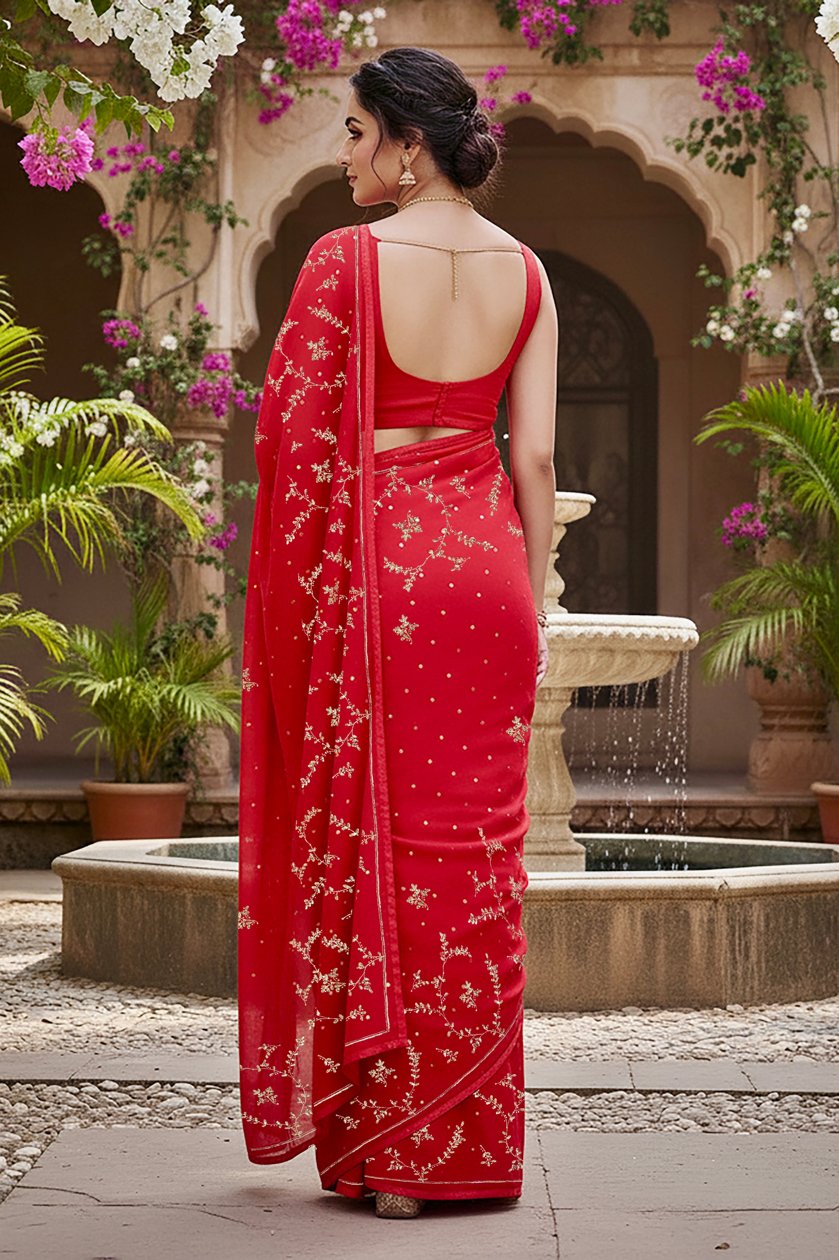 A model wearing a vibrant red gulmohar glow saree by umaid couture, standing in a garden courtyard