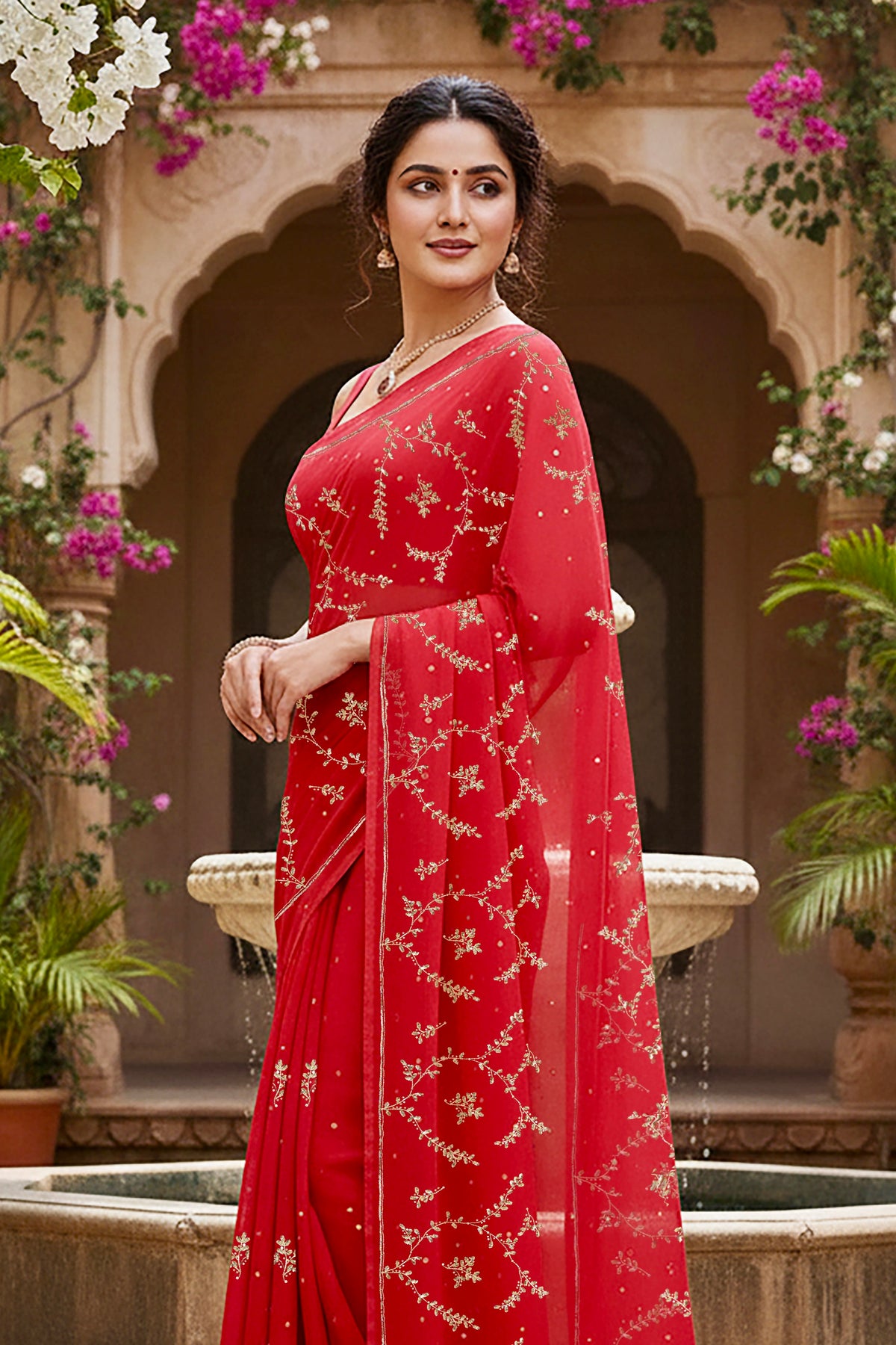 A model wearing a vibrant red gulmohar glow saree by umaid couture, standing in a garden courtyard
