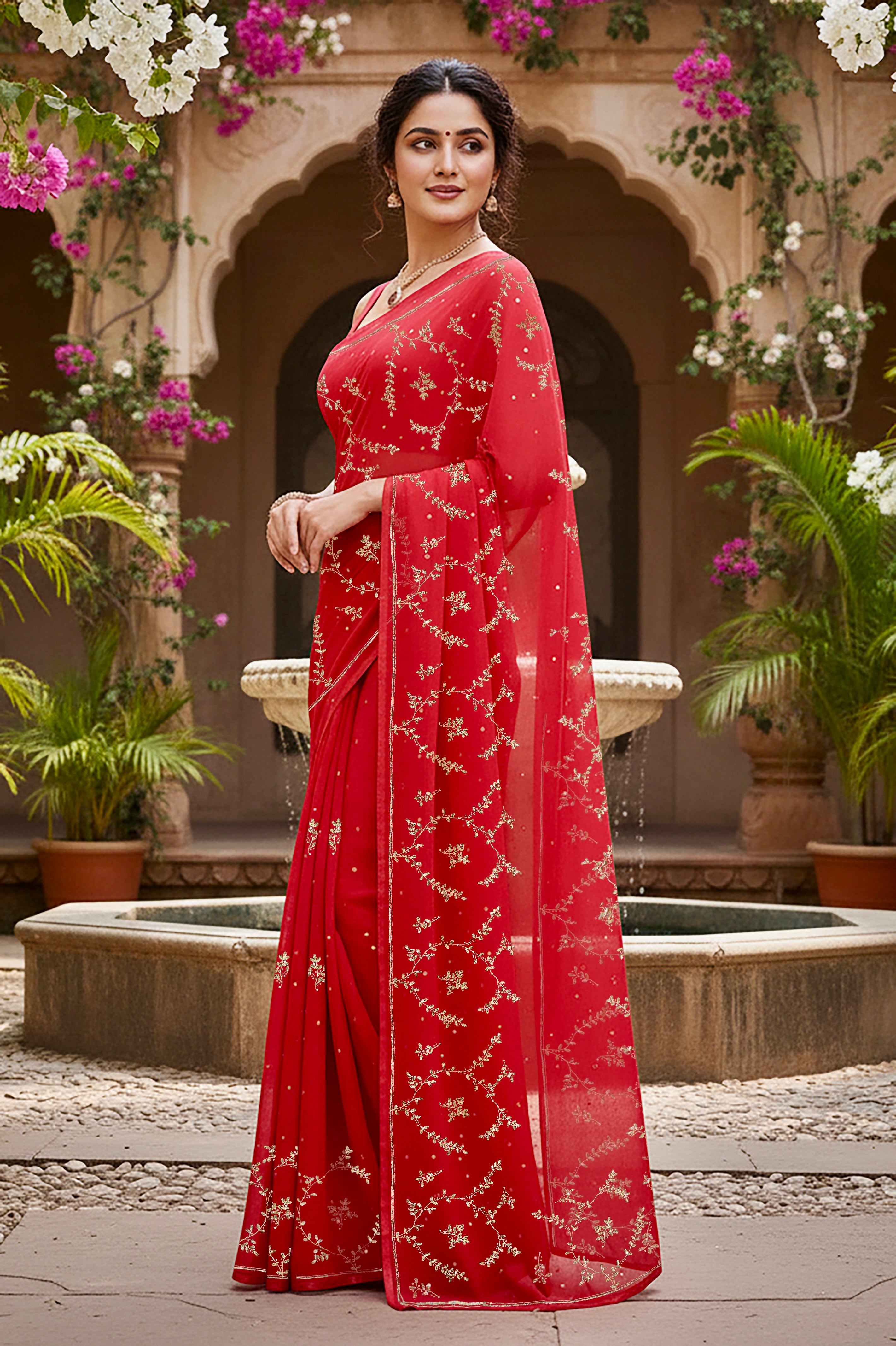 A model wearing a vibrant red gulmohar glow saree by umaid couture, standing in a garden courtyard