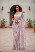 Woman in a light pink saree with floral  sequins patterns standing in an outdoor setting. The saree is by Umaid Couture