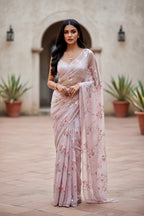 Woman in a light pink saree with floral  sequins patterns standing in an outdoor setting. The saree is by Umaid Couture